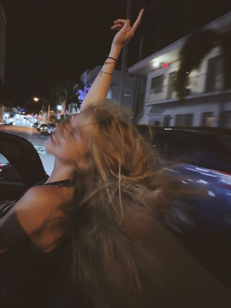 Jeune femme passant la tête par la fenêtre d’une voiture lors d’une soirée. 