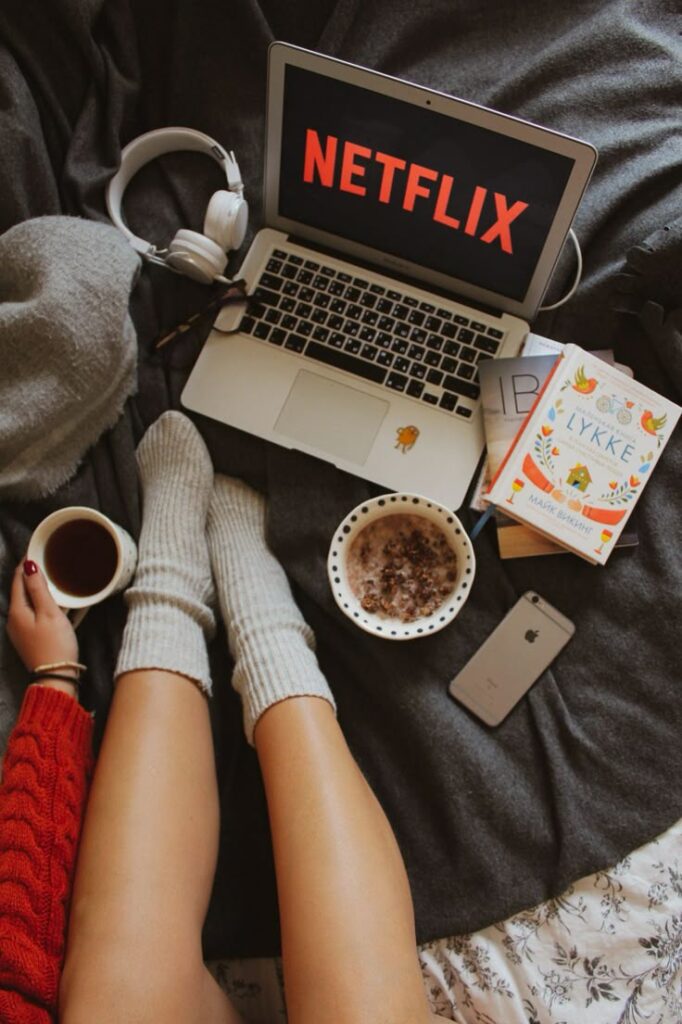Photo montrant un logo Netflix avec un bol de cereales, des livres sur un lit avec un plaid. Image illustrant la partie Devant mon écran, de la page À propos d’Emilie Barbe.